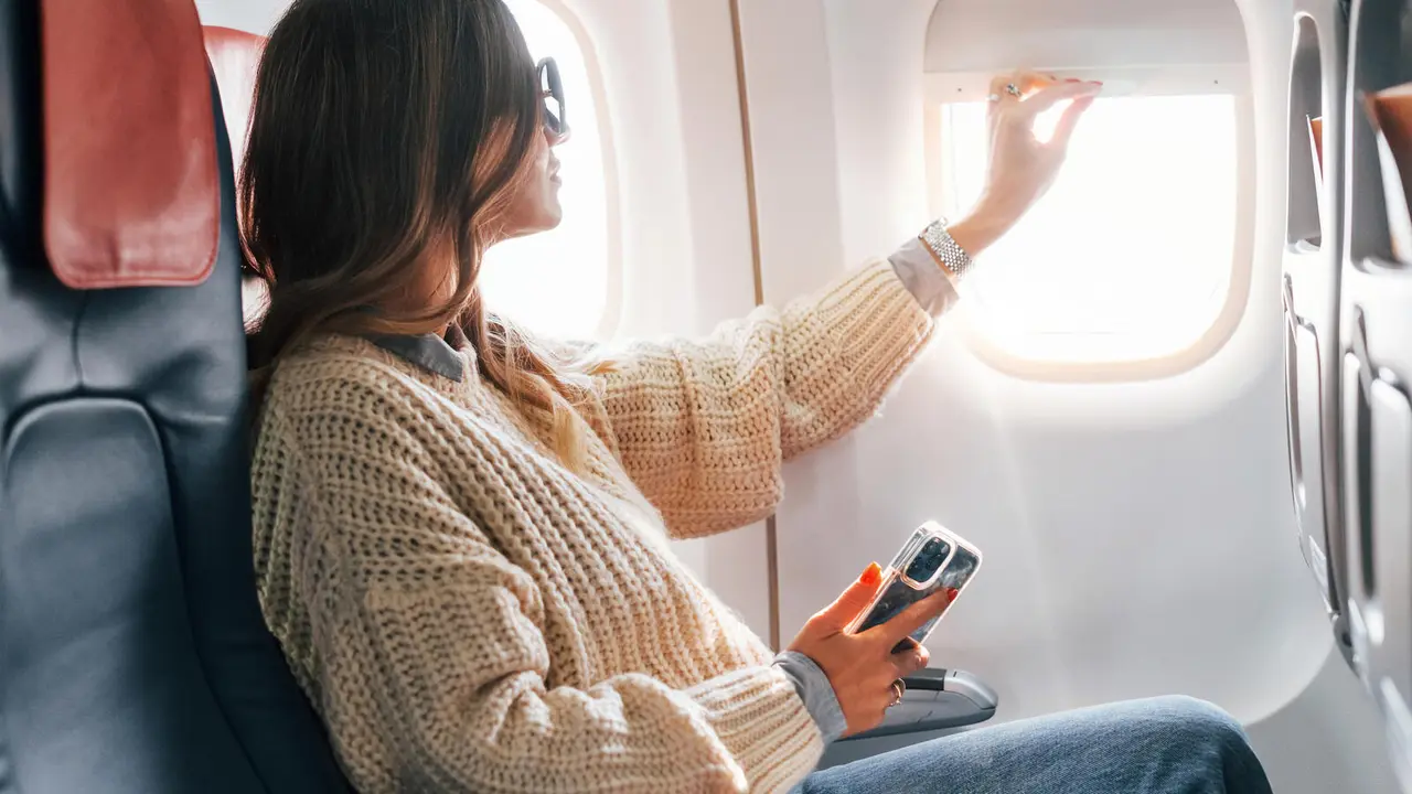 Sitting with phone in hands. Young female passanger in casual clothes is in the plane.
