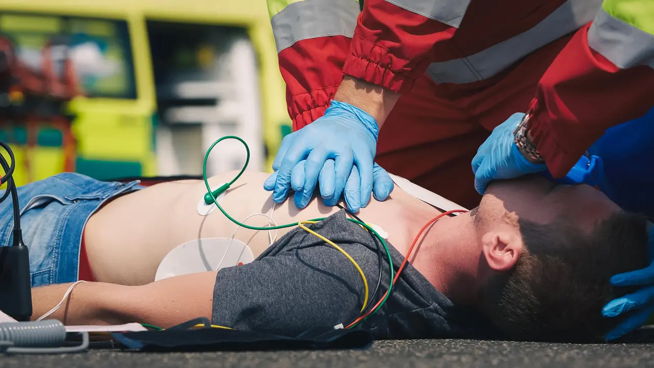 Hands of paramedic and doctor during resuscitation on road against ambulance car. Patient and team of emergency medical service. Themes rescue, urgency and health care.