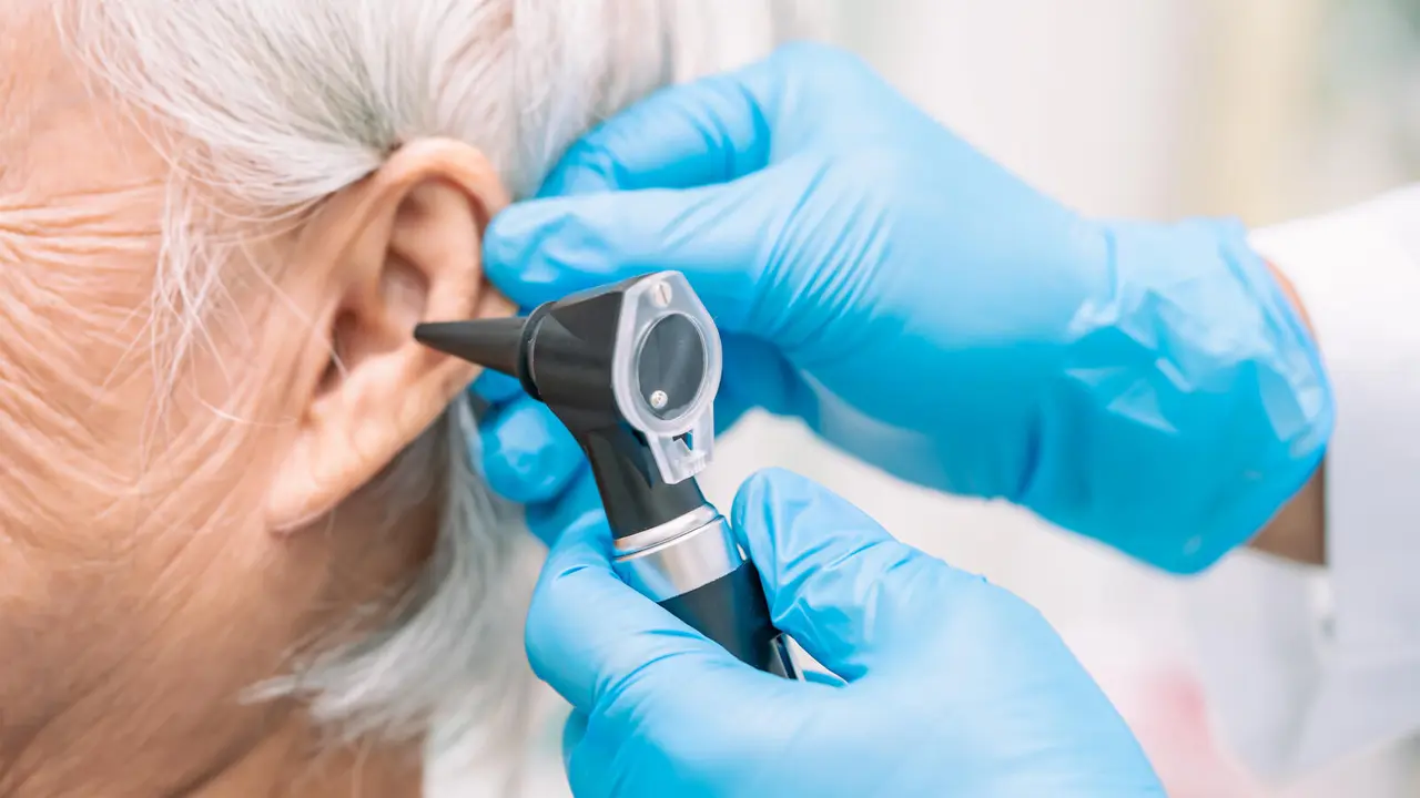 Audiologist or ENT doctor use otoscope checking ear of asian senior woman patient treating hearing loss problem.