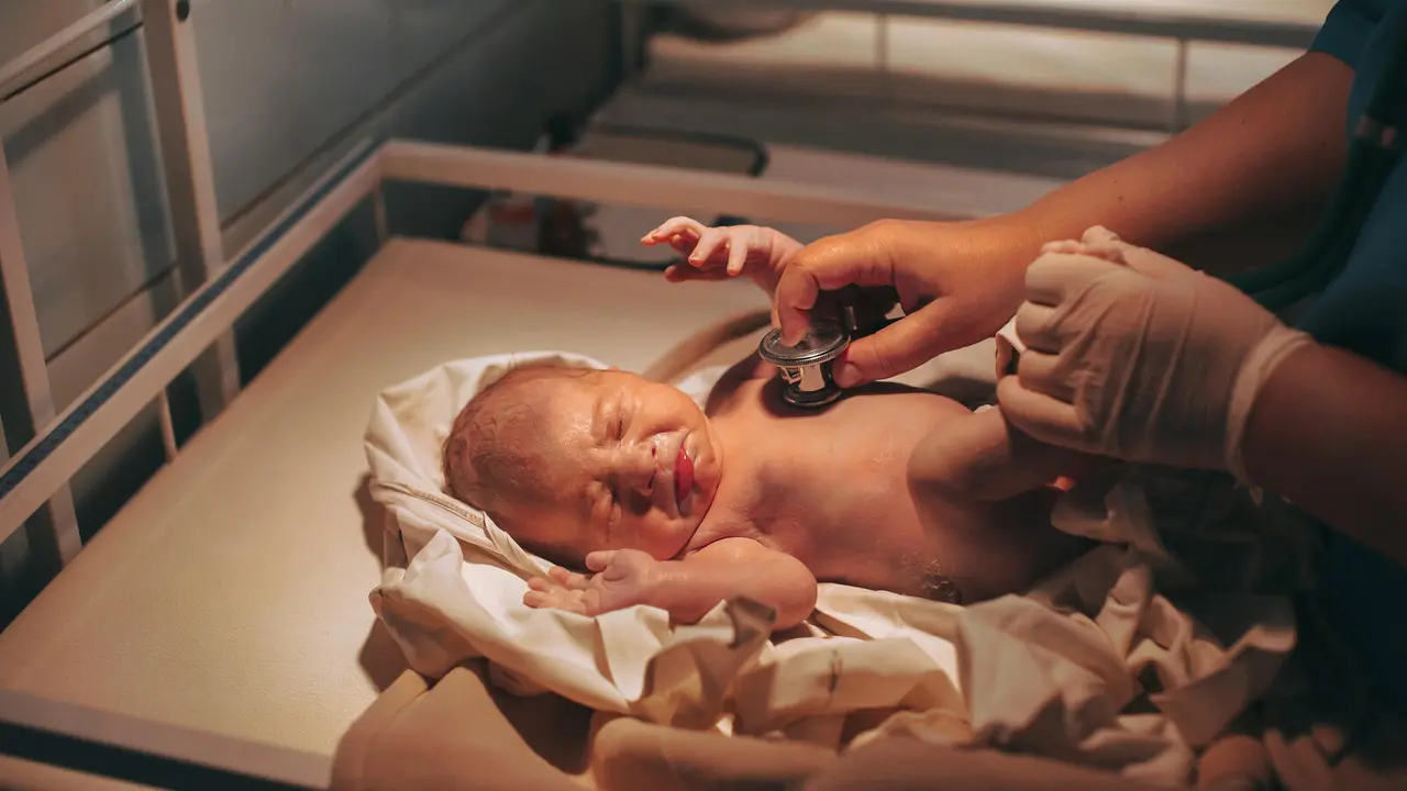 Doctor paediatrician examining baby in clinic, newborn baby crying in bed.